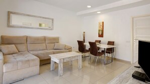 Ein Wohnzimmer mit Sofa, Couchtisch, Esstisch mit Stühlen, Fernseher und einer Tür.
