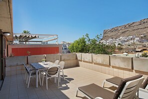 En takterrass med ett bord och stolar, en liten trädgård och utsikt över en stad som ligger på en sluttning.
