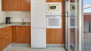 Eine Küche mit Holzschränken, einem weißen Kühlschrank, einer Mikrowelle und einem Backofen.