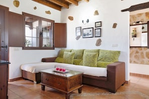 A room with a bed, a wooden nightstand, a glass coffee table, a brown sofa, and a stone wall.
