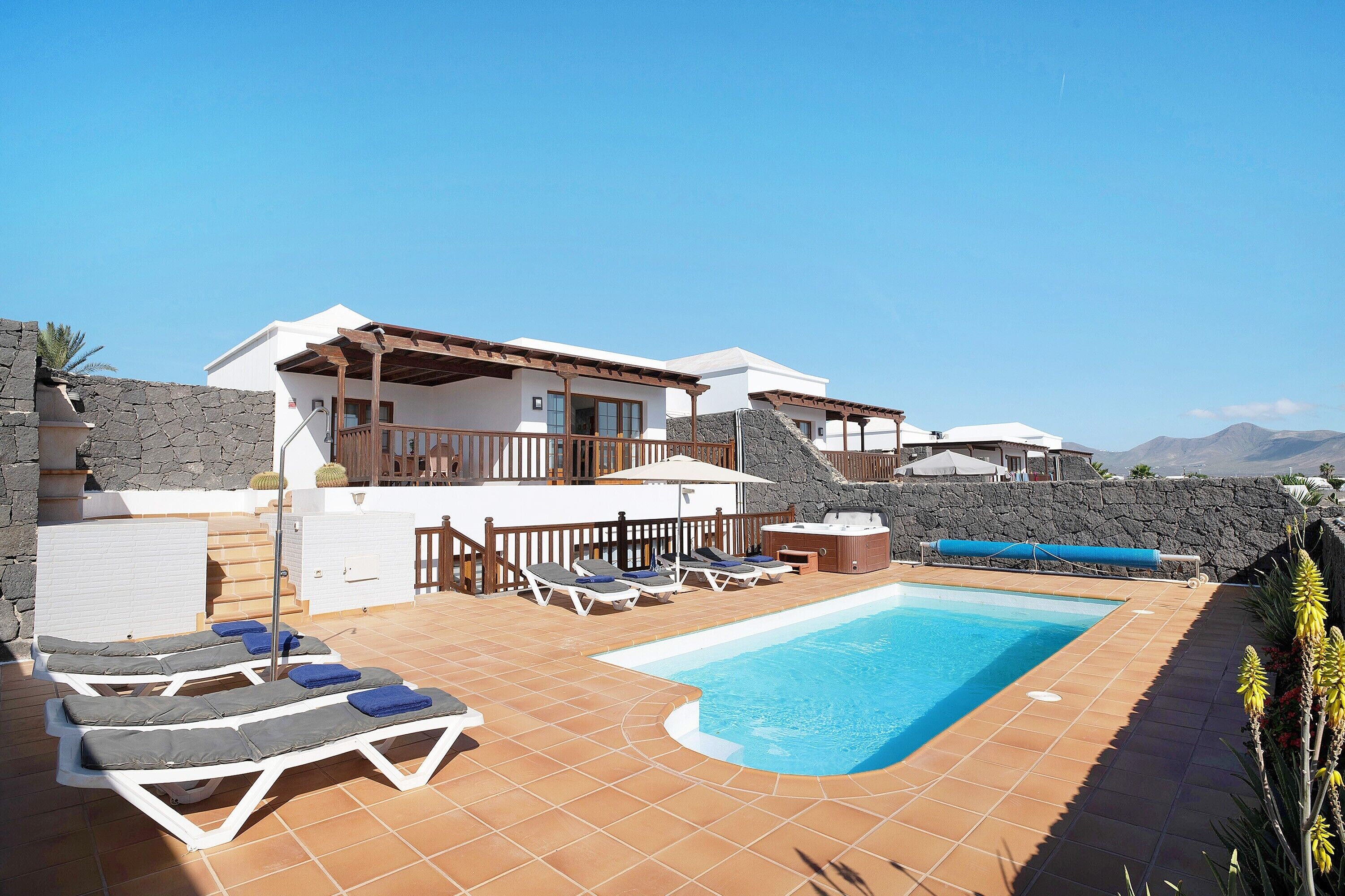 A modern villa with a swimming pool, sun loungers, and a stone wall.