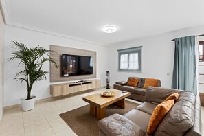 Una sala de estar moderna con un televisor de pantalla plana, una mesa de centro de madera, un sofá de cuero, una planta en maceta y una ventana con cortinas.