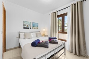 Una habitación de hotel con cama, mesita de noche, lámpara y ventana con cortinas.