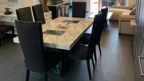 Un comedor moderno con una mesa de mármol, sillas oscuras, un televisor y una planta.