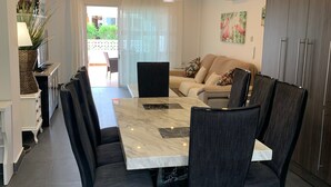 Un moderno comedor con una mesa de mármol y sillas oscuras, un sofá con cojines, y una zona de cocina con armarios y un refrigerador.