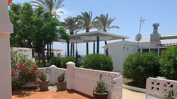 Un patio con plantas en macetas, una valla blanca y vistas al mar.