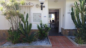 Entrada de un edificio con un jardín de cactus, un cartel con números y una puerta que da al interior.