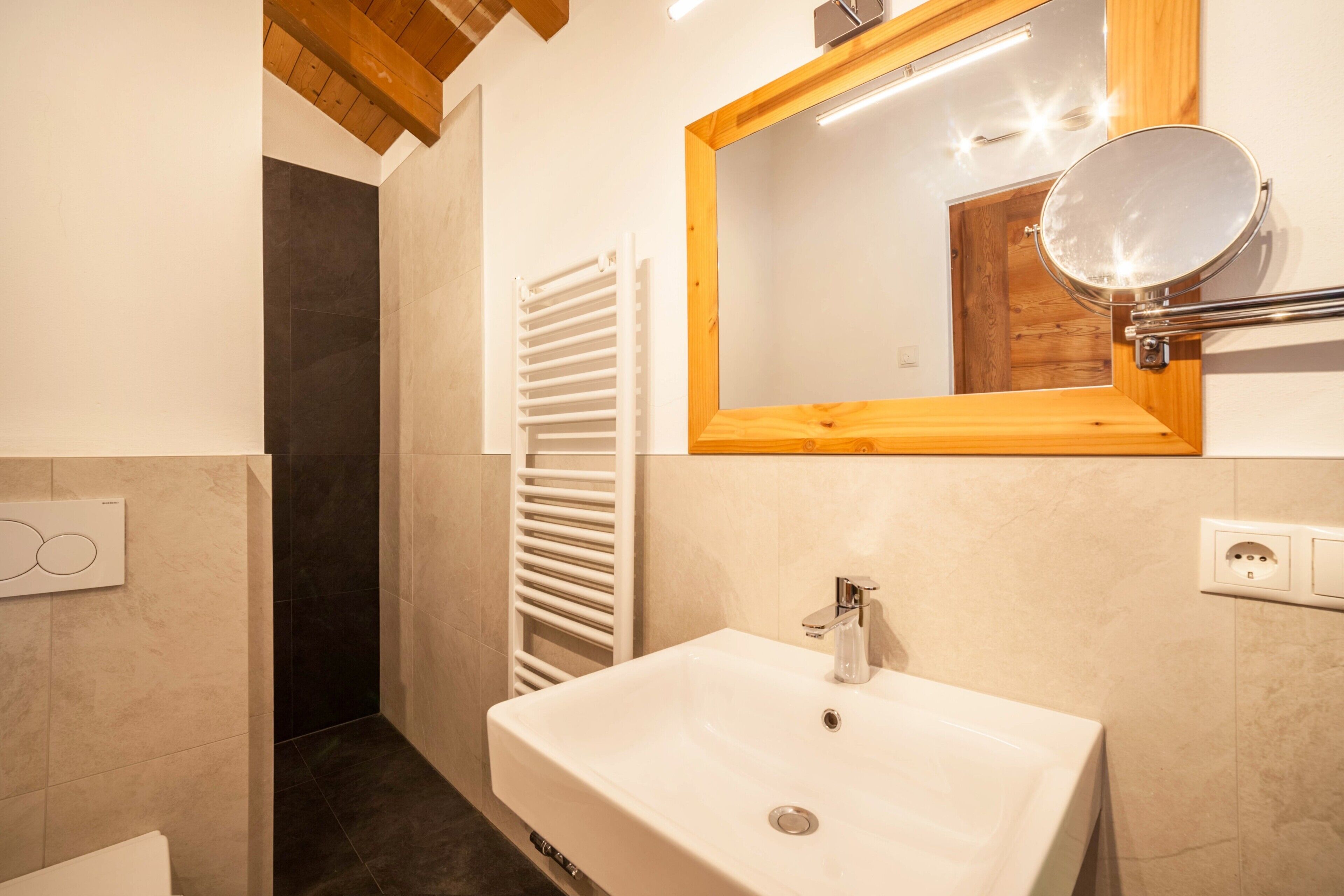 A bathroom with a white sink, a wooden-framed mirror, a towel rack, and a shower area.