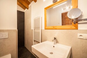 Ein Badezimmer mit einem weißen Waschbecken, einem spiegel mit Holzrahmen, einem Handtuchhalter und einer Duschkabine.