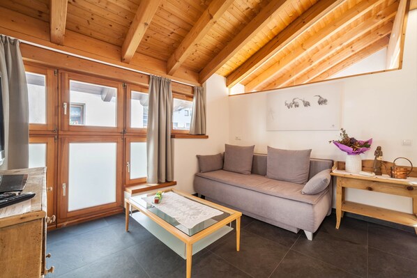 Ein Wohnzimmer mit einer Couch, einem Couchtisch, Holzbalken, großen Fenstern und einer Wand mit Kunstwerken.