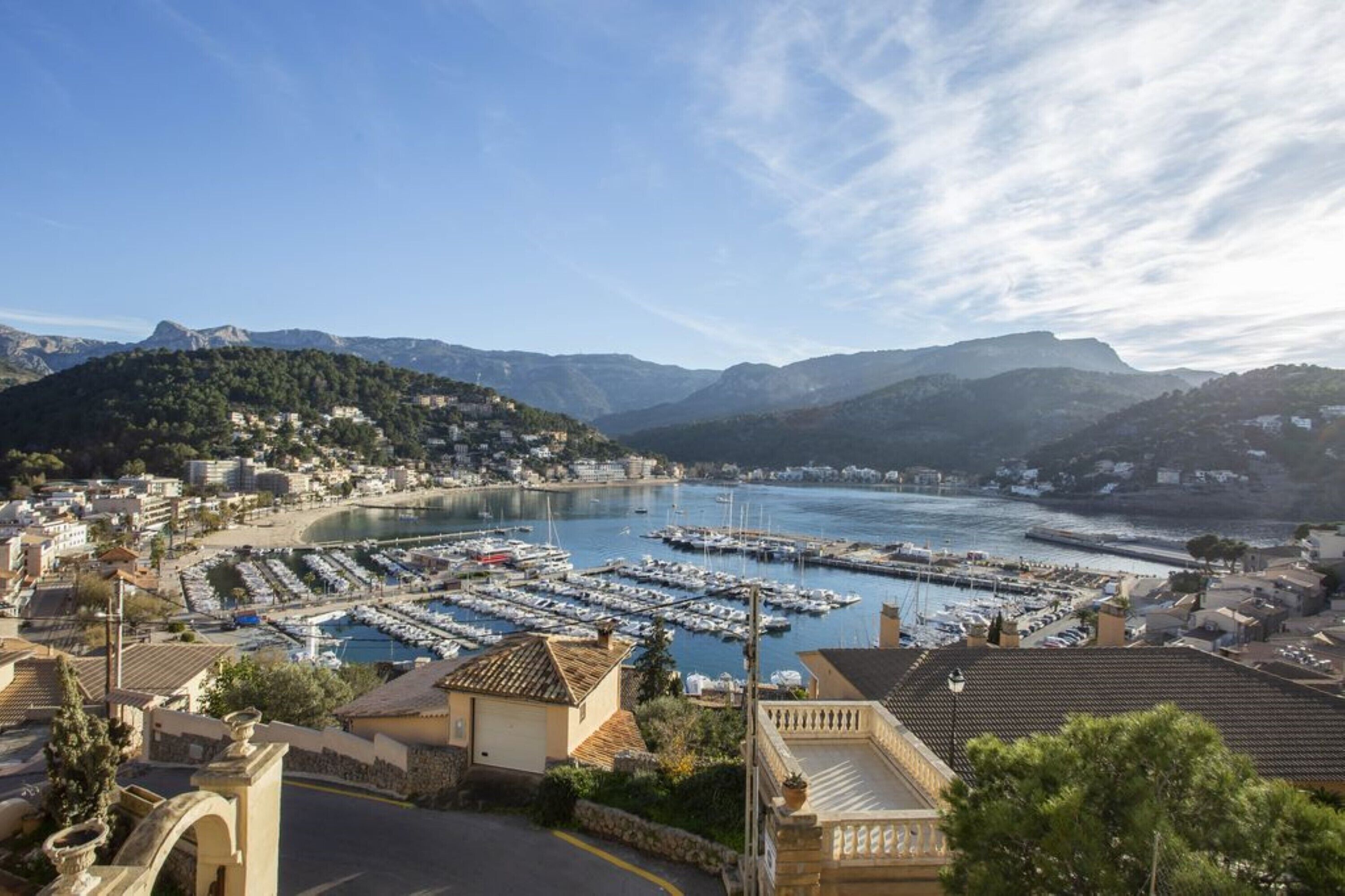 A coastal town with a marina, buildings, and mountains in the background.