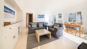 A modern living room with a sofa set, a coffee table, and a dining area with wooden chairs and a table. - Holiday Apartment Ponent with Sea View, Mountain View, Balcony, Terrace & Pool (Puerto de Sóller)