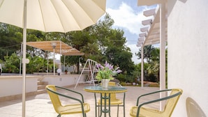 Une terrasse extérieure avec une table et des chaises, un grand parasol et une plante en pot.