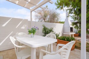 A patio with a white table and chairs, potted plants, and a white fence.