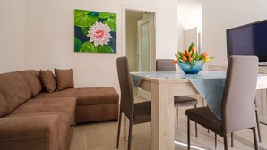 Un salon avec un canapé, une table à manger et des chaises, un téléviseur et un tableau représentant des fleurs.
