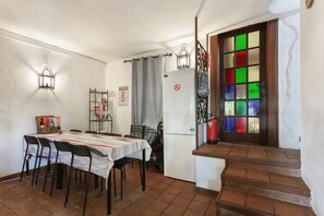 A dining area with a table set for four, a refrigerator, a fire extinguisher, and a staircase leading to a door with colorful glass panels.