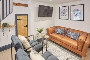 A modern living room with a leather sofa, a glass coffee table, a TV mounted on the wall, and framed artwork. - Host & Stay | Grumbles Cottage (Whitby)