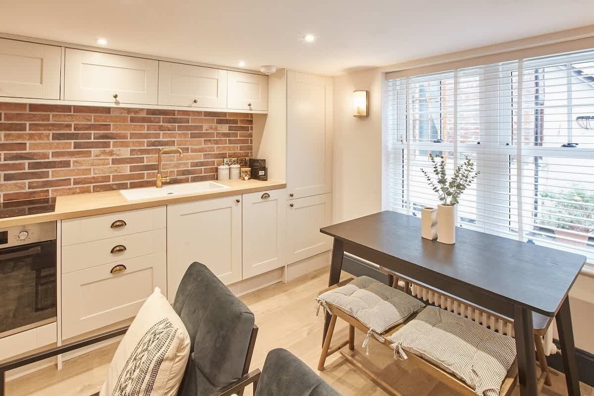 A kitchen with white cabinets, a brick backsplash, and a dining area with a table and chairs.