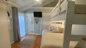 A bedroom with a bunk bed, a flat-screen TV, a door leading to another room, and a wooden floor. -  3 Ensuite Bedrooms - In-town Gem - Walk Everywhere - Sleeps 12 - Private Drive (Rehoboth Beach)