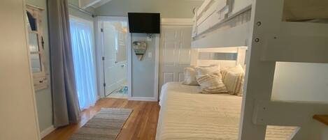 A bedroom with a bunk bed, a flat-screen TV, a door leading to another room, and a wooden floor.