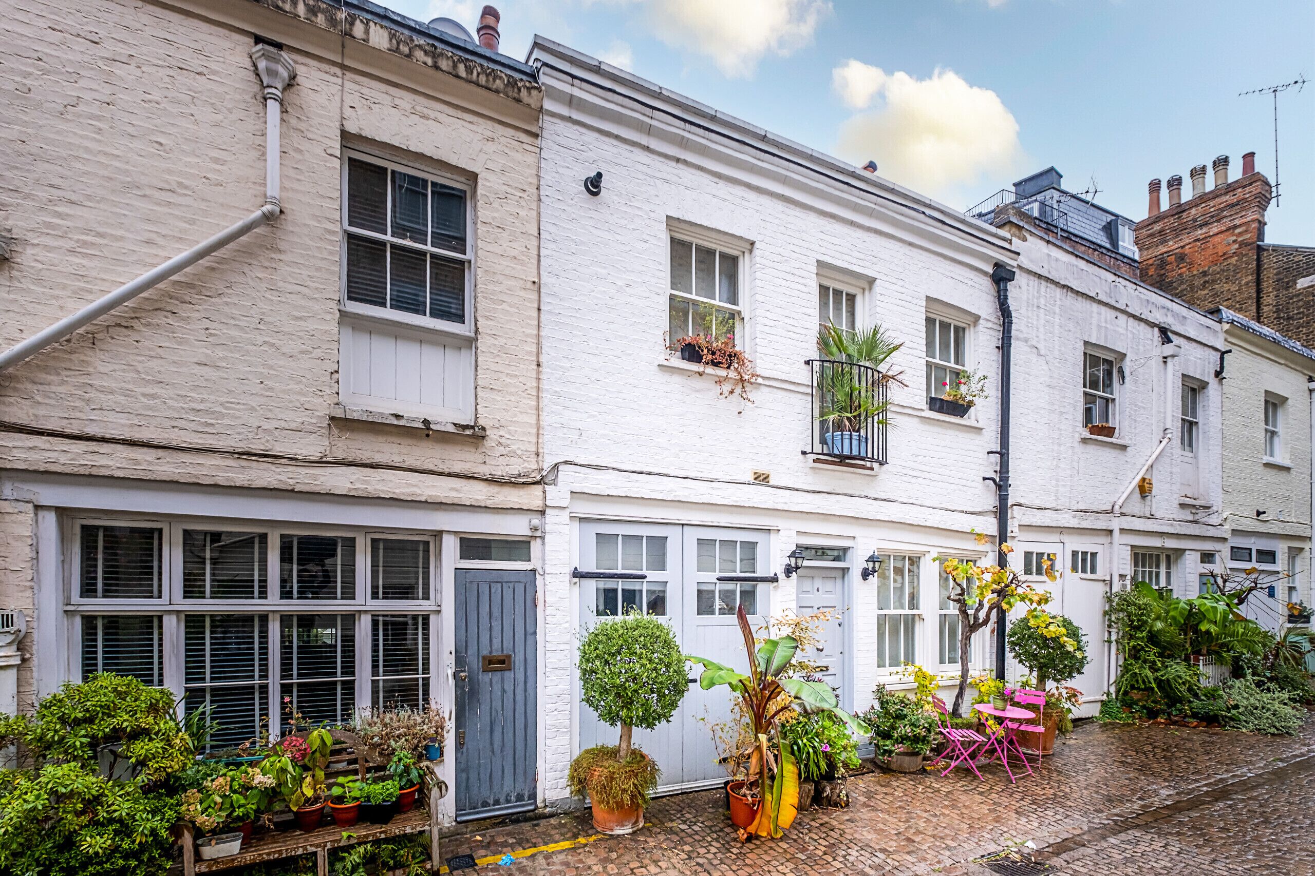 A row of white terraced houses with multiple windows and balconies, some with plants.