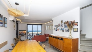 A modern living room with a wooden dining table, red sofa, and a view of the sea through large windows.