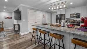 Una cocina moderna con encimera de granito, electrodomésticos de acero inoxidable y taburetes de bar.