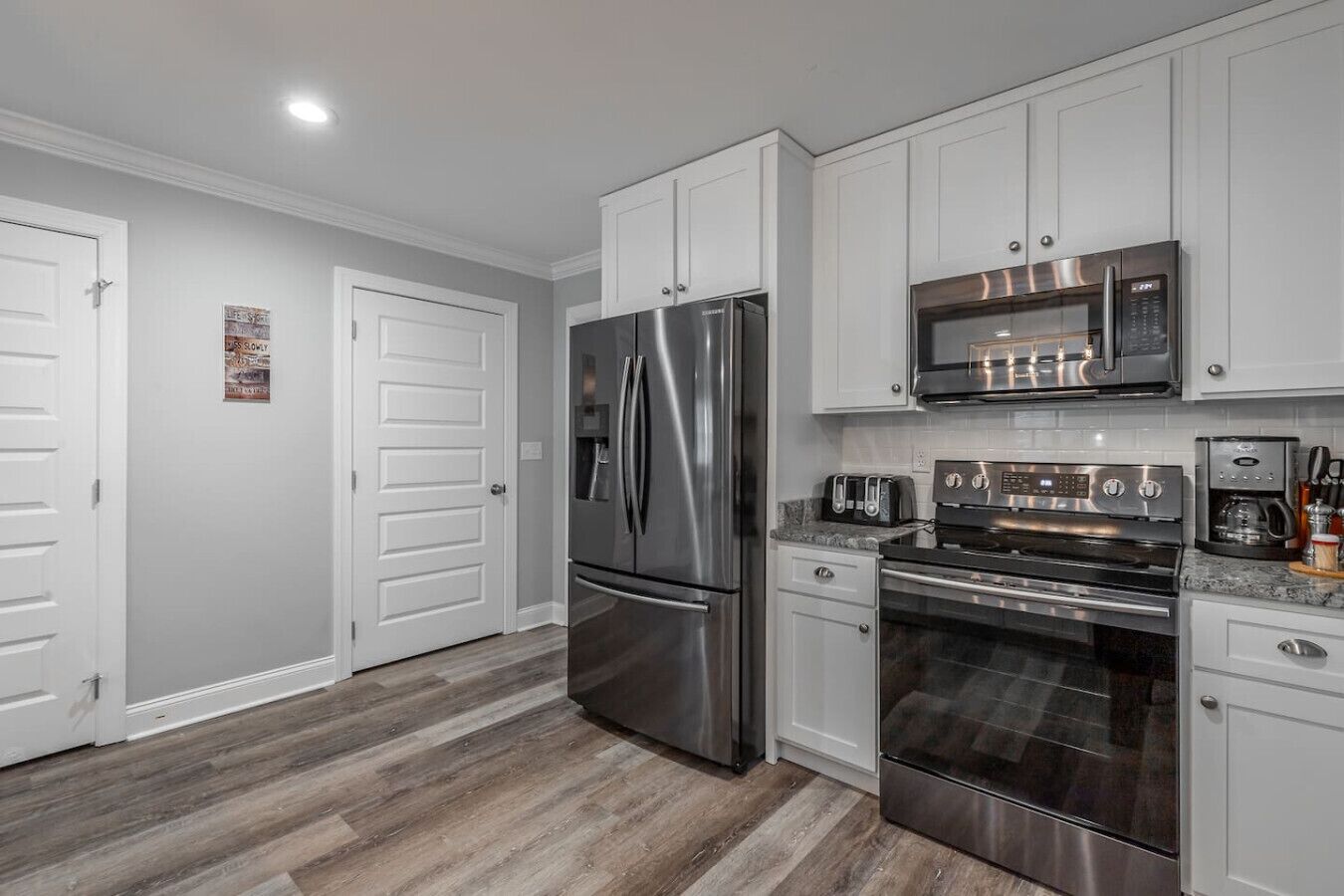 Una cocina moderna con electrodomésticos de acero inoxidable, armarios blancos y piso de madera.