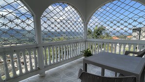 Un balcon abrité, doté d’une table et de chaises, de balustrades blanches et offrant une vue sur le paysage.