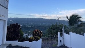 Un bâtiment blanc avec une entrée fermée par un portail, une vue sur des montagnes lointaines et un ciel dégagé.
