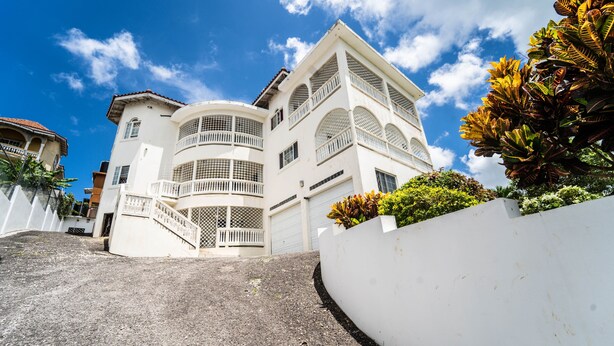 A multi-story white building with balconies, a curved driveway, and a white wall with plants. - Skyline Suites, Breathtaking Mountains & City View 1 Bedroom Apts by RedAwning (Montego Bay)