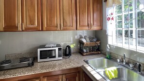 A kitchen with wooden cabinets, a microwave, a stove, and a sink. - Skyline Suites, Breathtaking Mountains & City View 1 Bedroom Apts by RedAwning (Montego Bay)