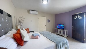 A hotel room with a bed, a TV, a door, and an air conditioning unit. - Skyline Suites, Breathtaking Mountains & City View 1 Bedroom Apts by RedAwning (Montego Bay)