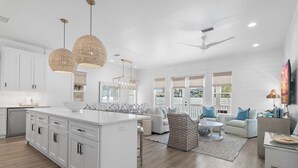 Une cuisine spacieuse avec des meubles blancs, un grand îlot central et des luminaires suspendus.