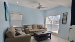 Ett vardagsrum med en beige soffa, ett soffbord och en takfläkt.