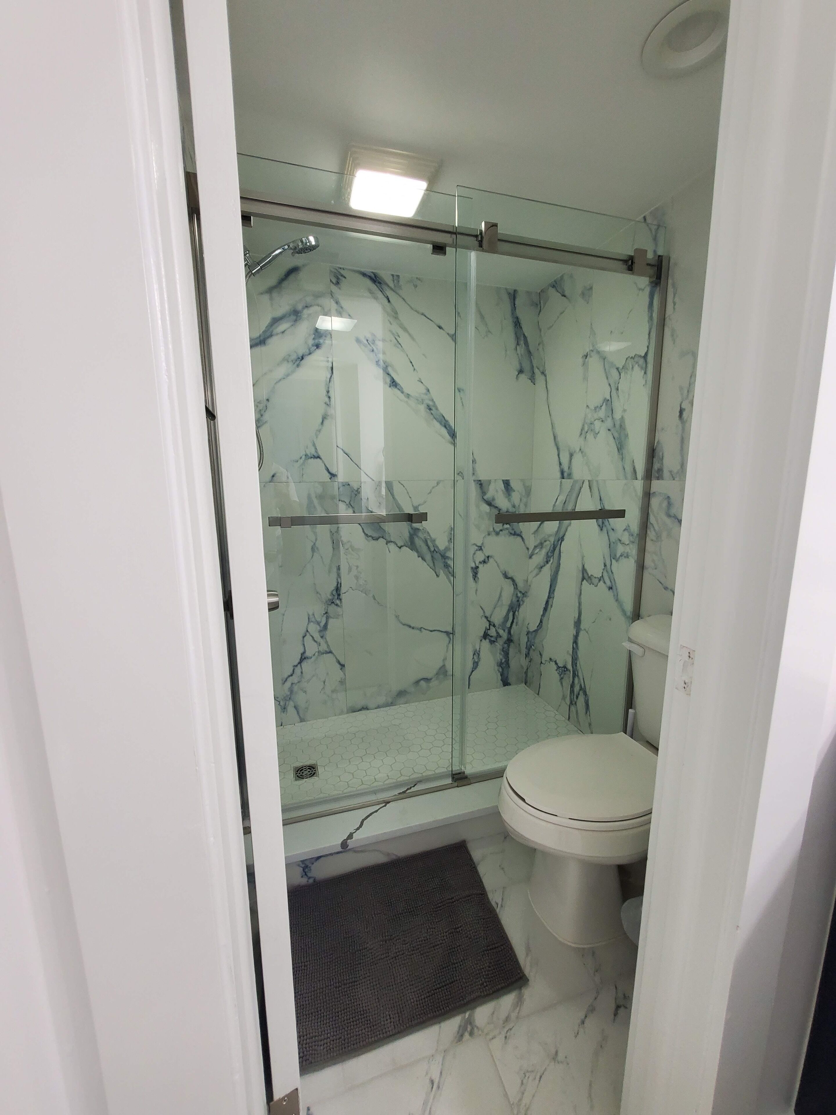 A bathroom with a glass-enclosed shower, a toilet, and a marble floor.