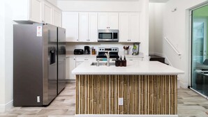 A modern kitchen with white cabinets, stainless steel appliances, a central island, and a glass door leading to a balcony. - Rum Runners and Margaritas (Kissimmee)