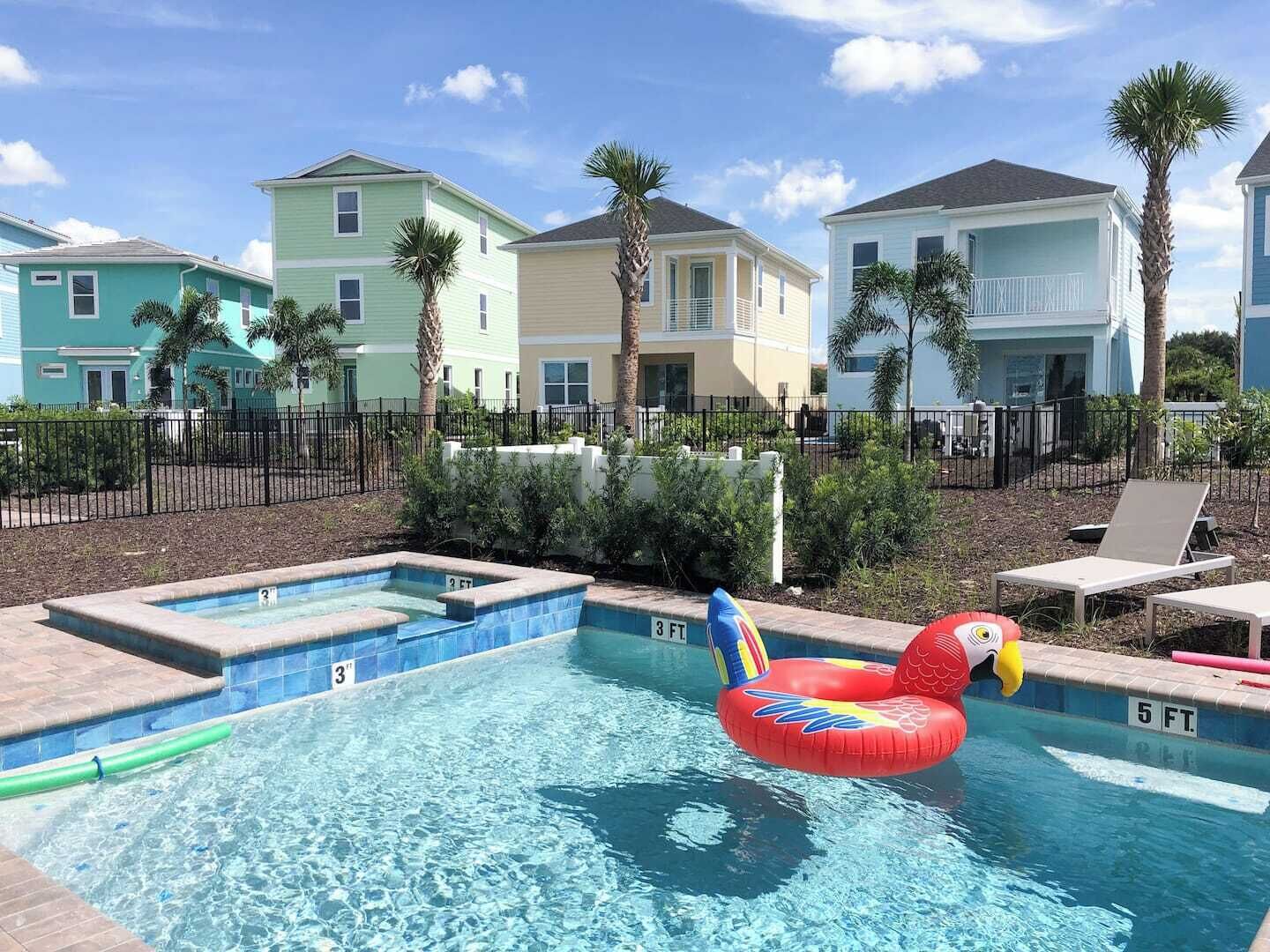 A swimming pool with a floating toy, surrounded by a fence, with houses in the background.