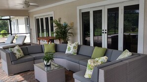 A covered patio area with a grey sectional sofa, a glass coffee table, and a potted plant.