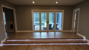 A spacious room with wooden flooring, a sliding glass door leading to an outdoor patio, and a built-in light strip along the baseboards.