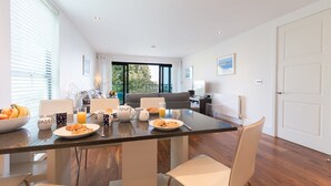 A modern kitchen with a large island, dining table, and chairs. There are breakfast items on the table, and a view of the outdoors through the windows.