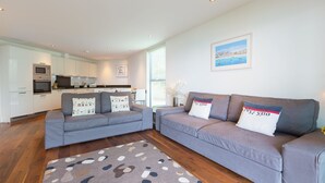 A modern living room with a grey sofa set, a patterned rug, and a kitchen in the background.