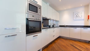 A modern kitchen with white cabinets, stainless steel appliances, and a wooden floor.