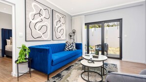 A modern living room with a blue sofa, a round coffee table, and abstract wall art. - Spacious | Brand New | 2 Bed | Rosebank (Johannesburg)