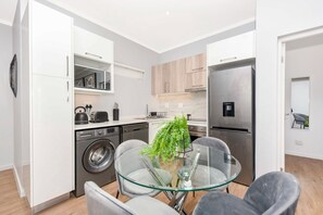 A modern kitchen with a built-in washing machine, a glass dining table, and a refrigerator.