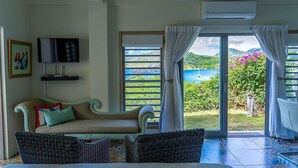 A room with a sofa, a television, and a view of a coastal landscape through a sliding glass door. - STARLIGHT: GORGEOUS VIEWS OF THE BEACH, FORT BERKLEY & MONTSERRAT (English Harbour)