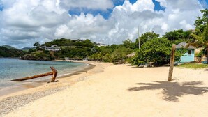 A beach with a wooden post, a house, and a hill in the background. - STARLIGHT: GORGEOUS VIEWS OF THE BEACH, FORT BERKLEY & MONTSERRAT (English Harbour)