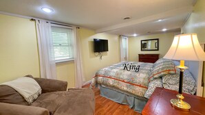 Een slaapkamer met een bed met het opschrift 'King', een houten dressoir, een aan de muur bevestigde televisie en een lamp op een nachtkastje.