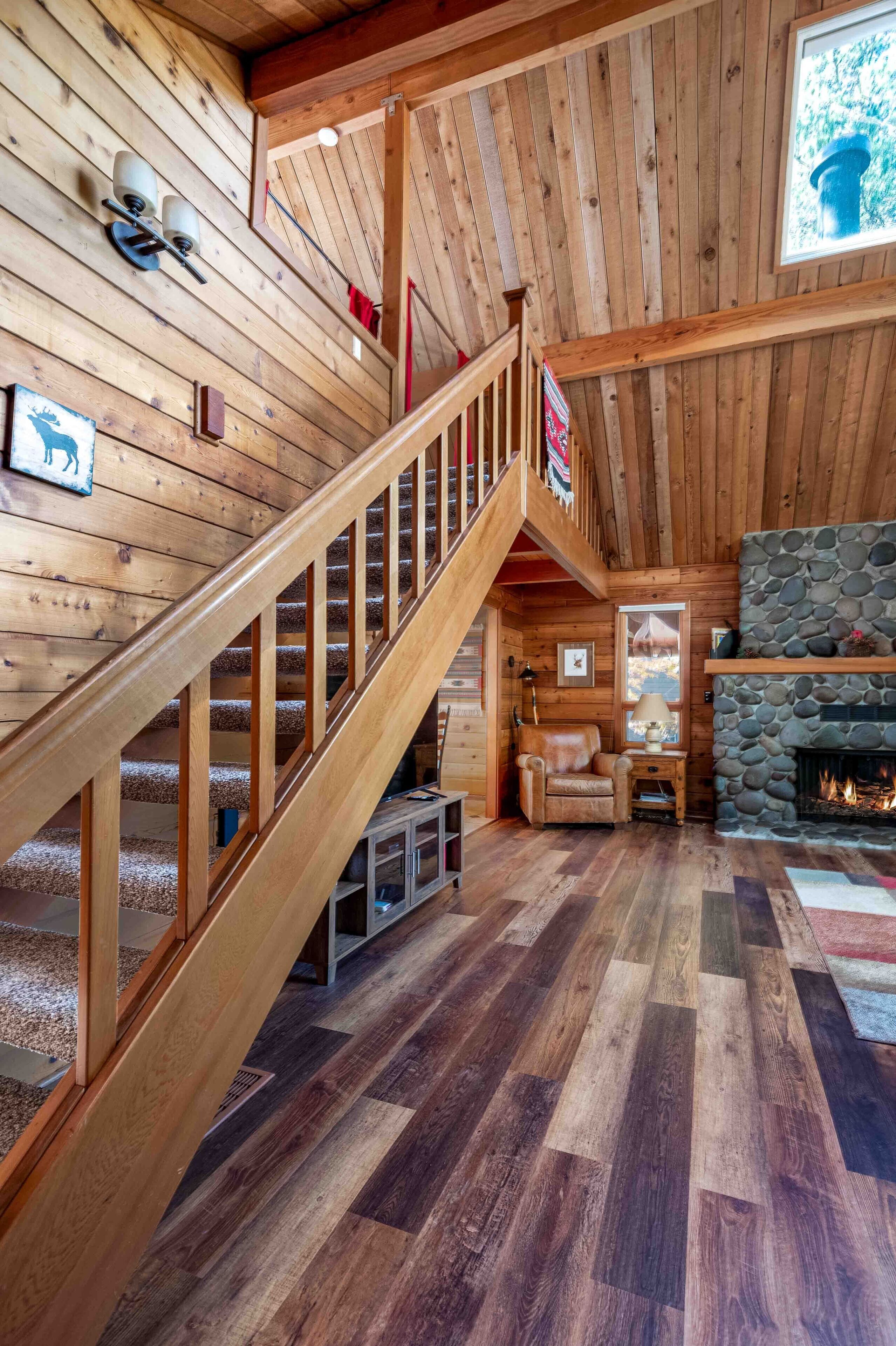 A wooden interior with a staircase, a stone fireplace, and a cozy seating area.