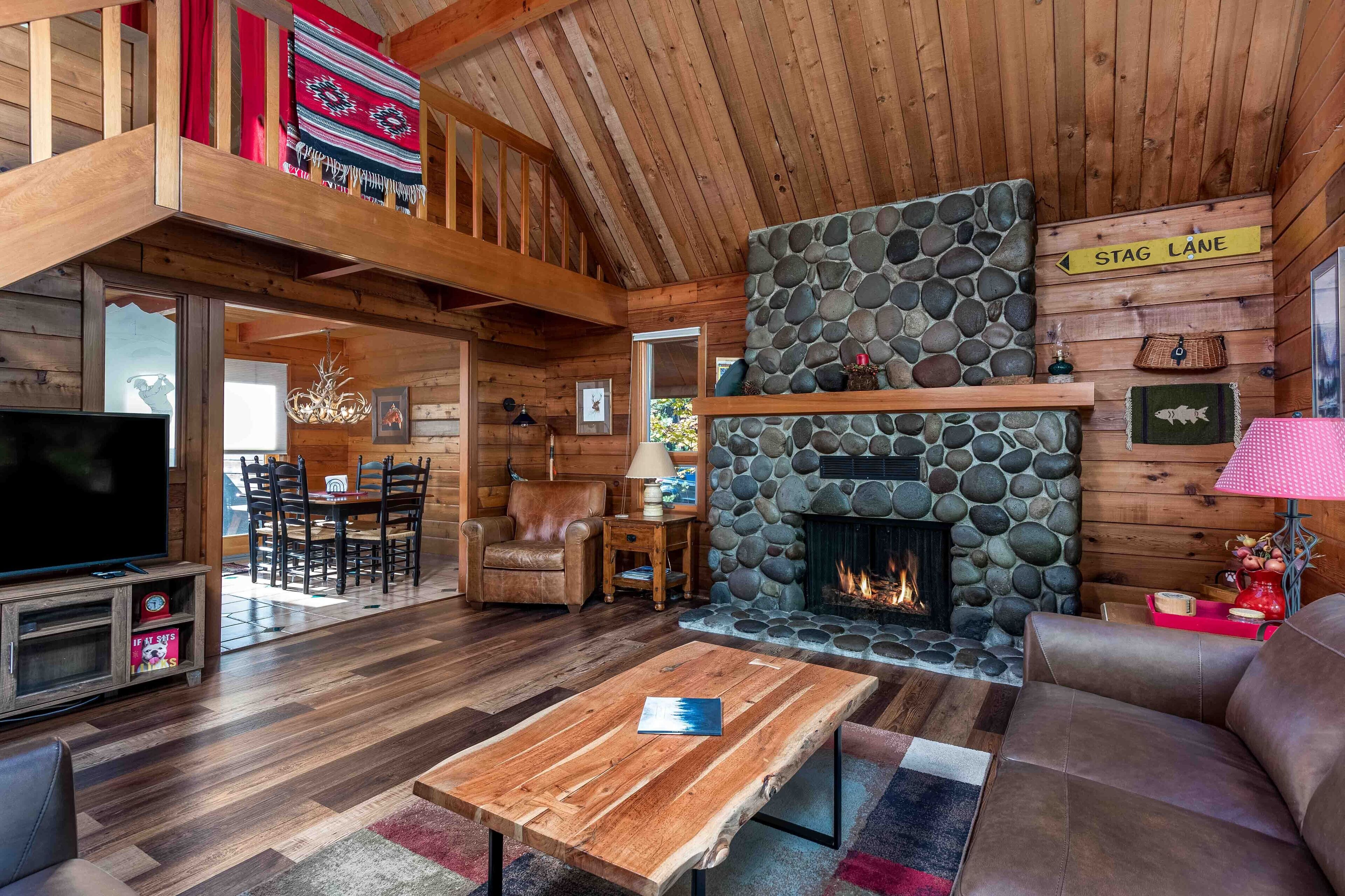 A cozy cabin interior with a stone fireplace, wooden furniture, and a television.